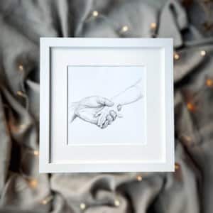 An older hand holding a child's hand pencil drawing in white square frame